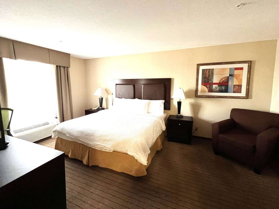 A hotel room with a large bed, two bedside tables with lamps, a chair, a desk with a computer, and a painting on the wall.
