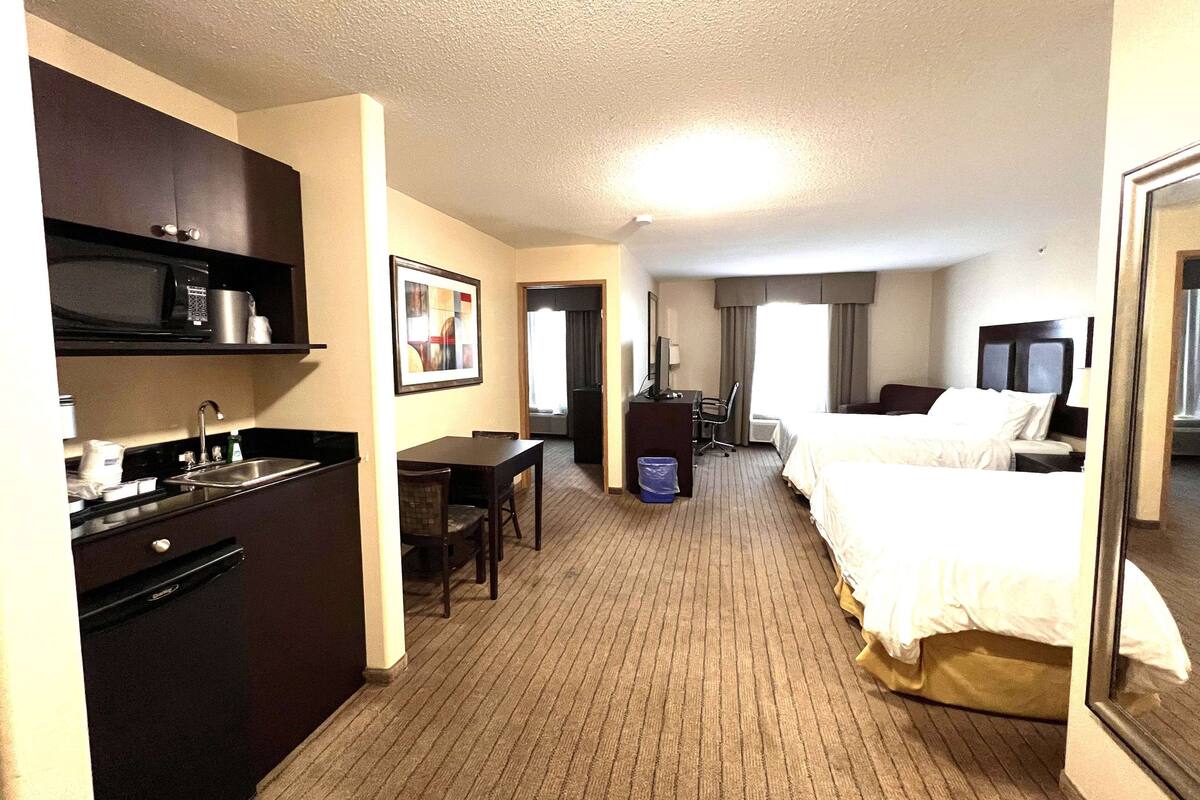 A hotel room with a kitchenette, a bed, a desk, and a large mirror.