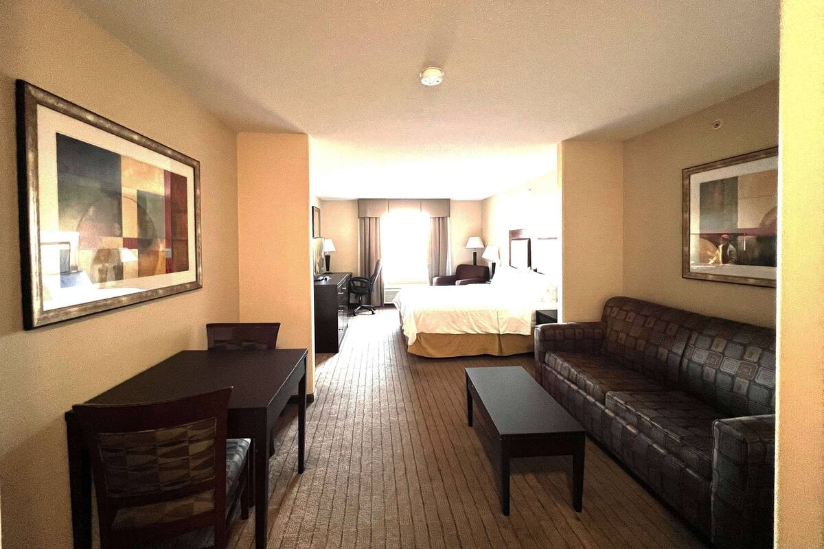 A hotel room with a bed, a sofa, a dining table, and a TV.