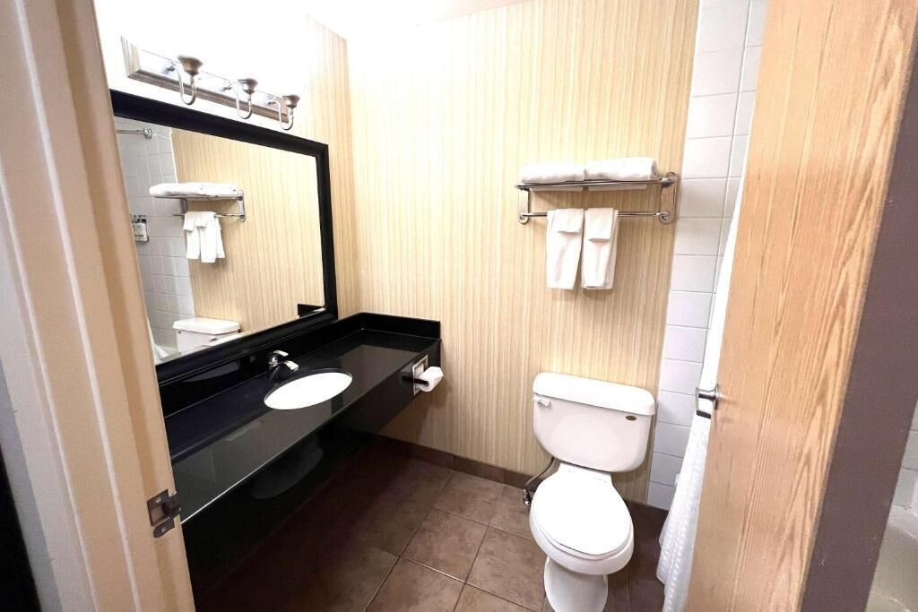 A modern bathroom with a black countertop, white sink, and toilet. There are towels hanging on the wall and a mirror above the sink.