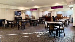 A hotel dining area with multiple tables and chairs, a television mounted on the wall, and a kitchen area in the background. - Ramada by Wyndham Prince Albert (Prince Albert)