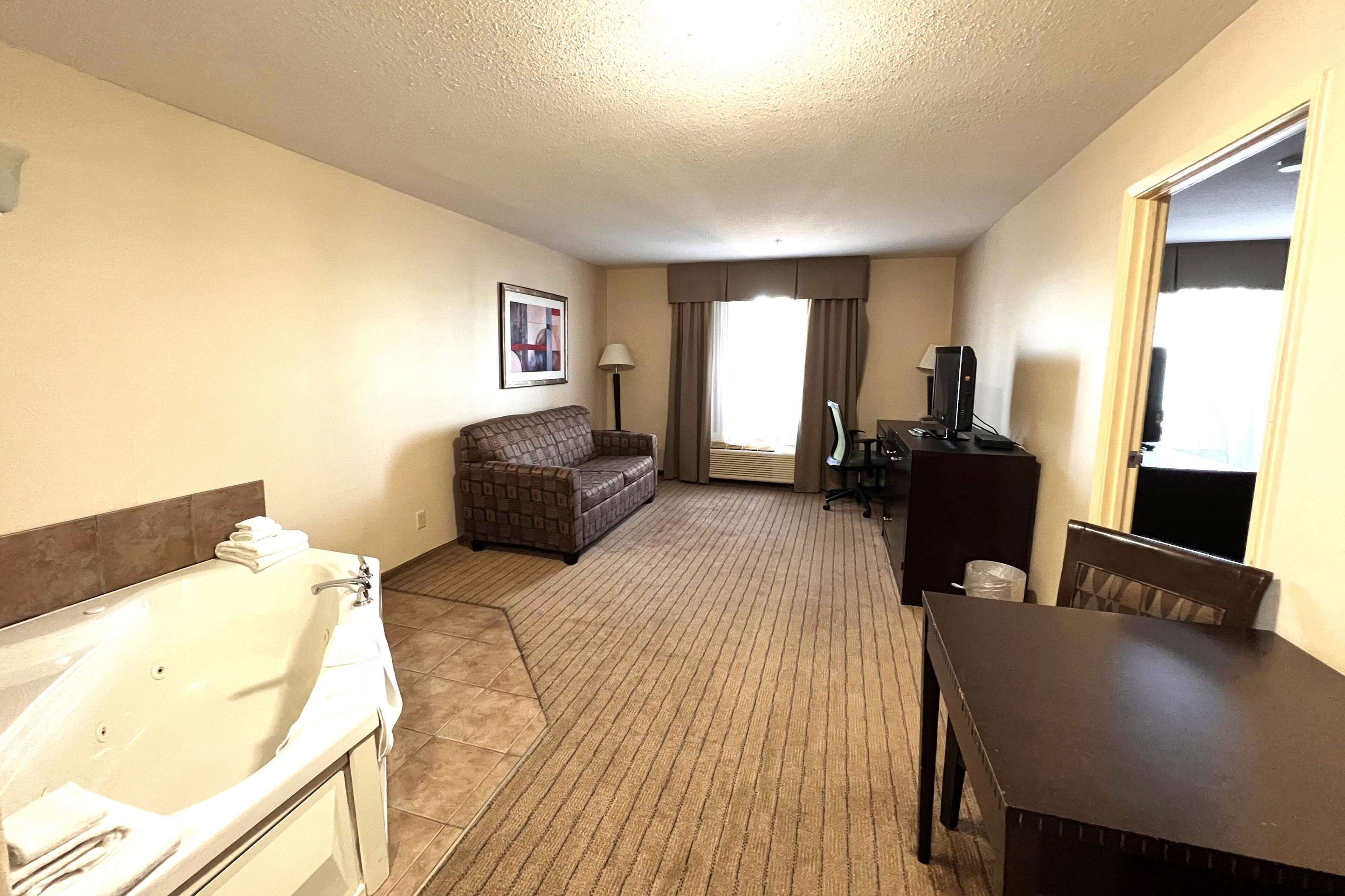 A hotel room with a large bathtub, a sofa, a dining table, and a TV.
