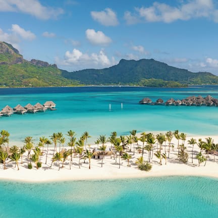 A beach resort with overwater bungalows, a sandy beach, and a mountain in the background.