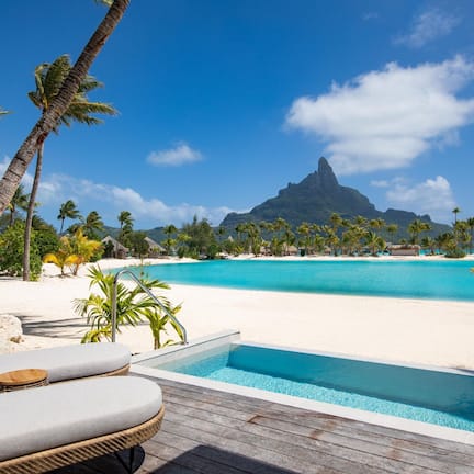 A poolside area with lounge chairs and a view of a beach and mountain.