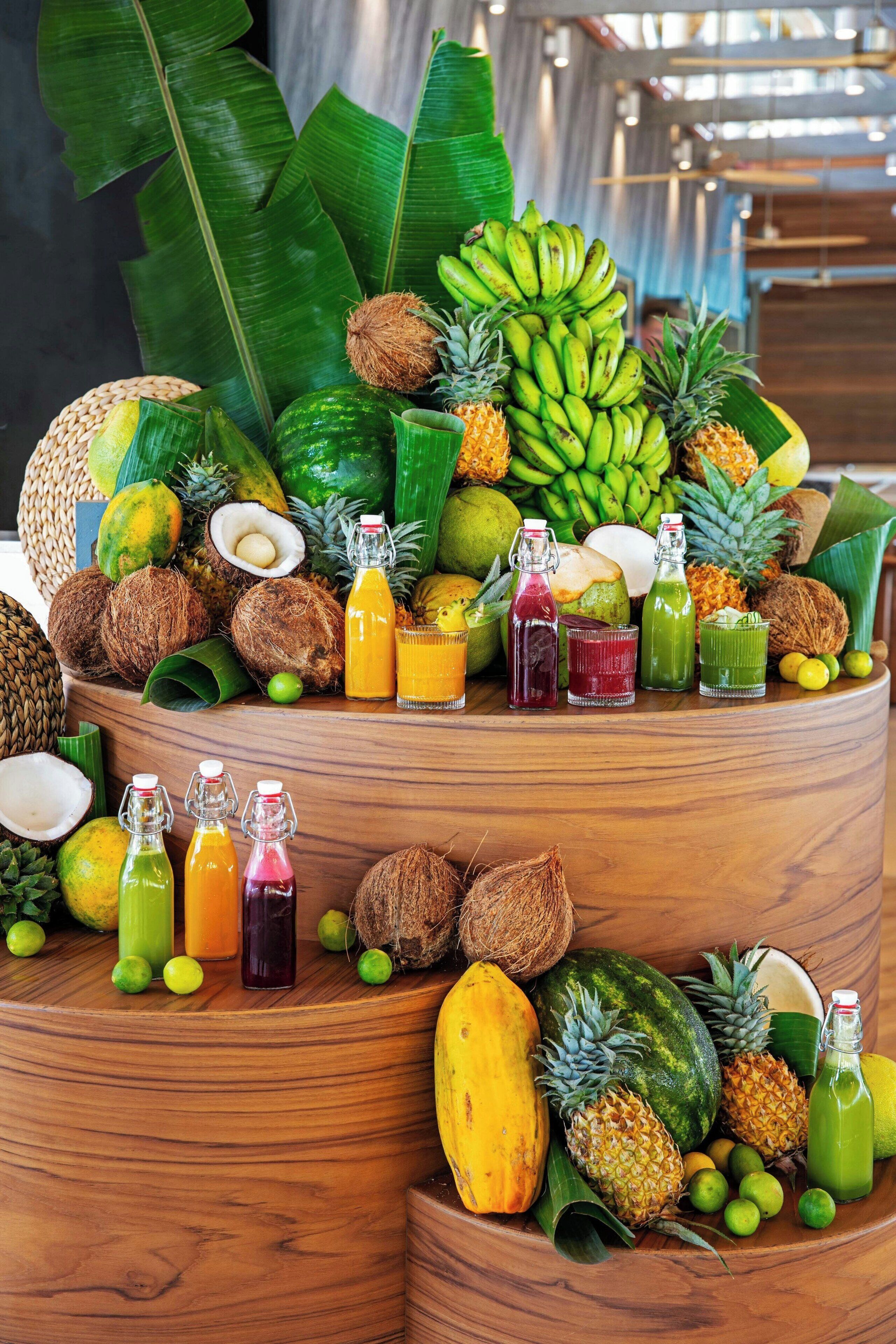 A wooden table with various tropical fruits and bottles of juice.