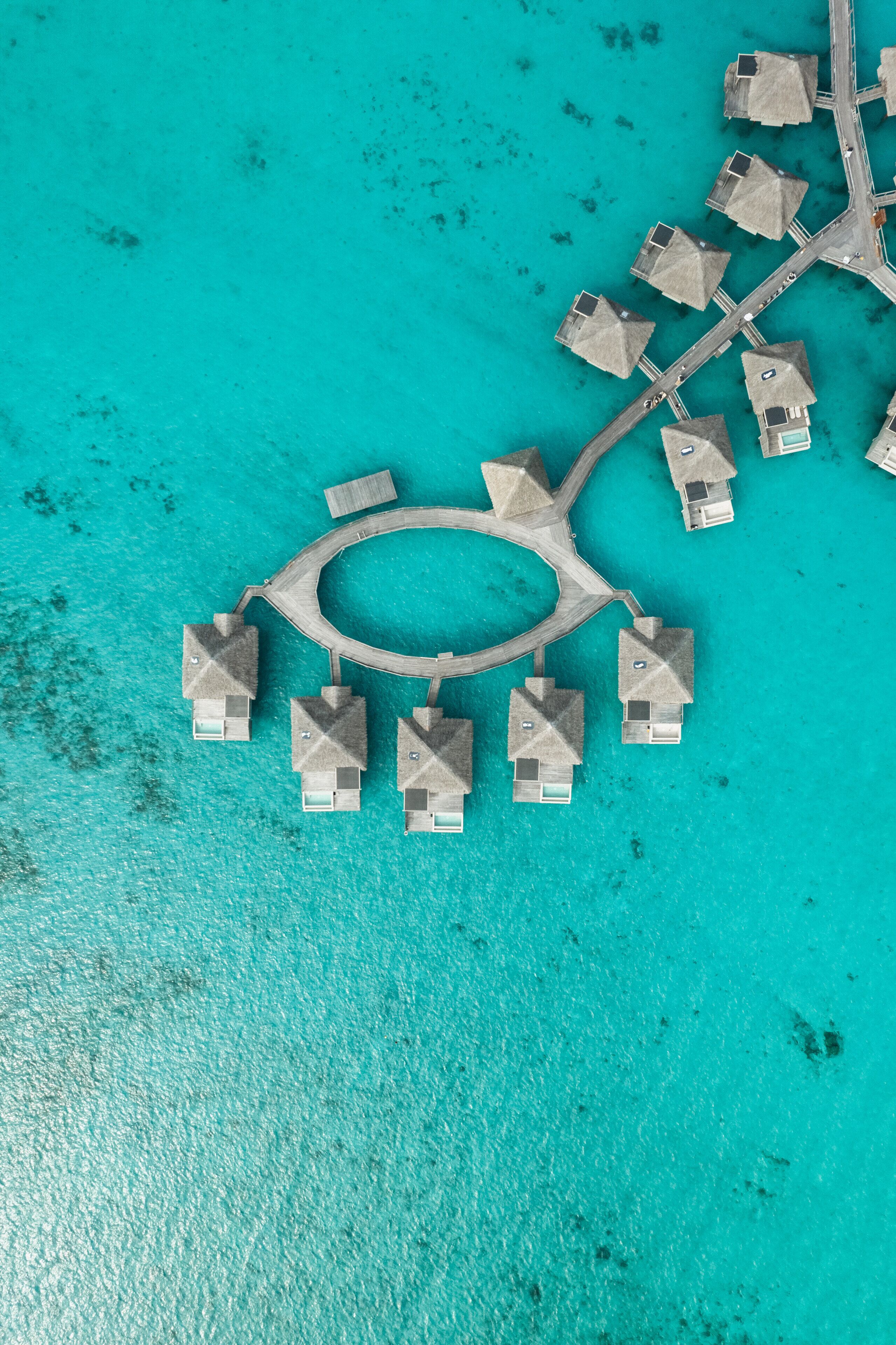 An aerial view of a resort with overwater bungalows arranged in a circular pattern around a central lagoon.