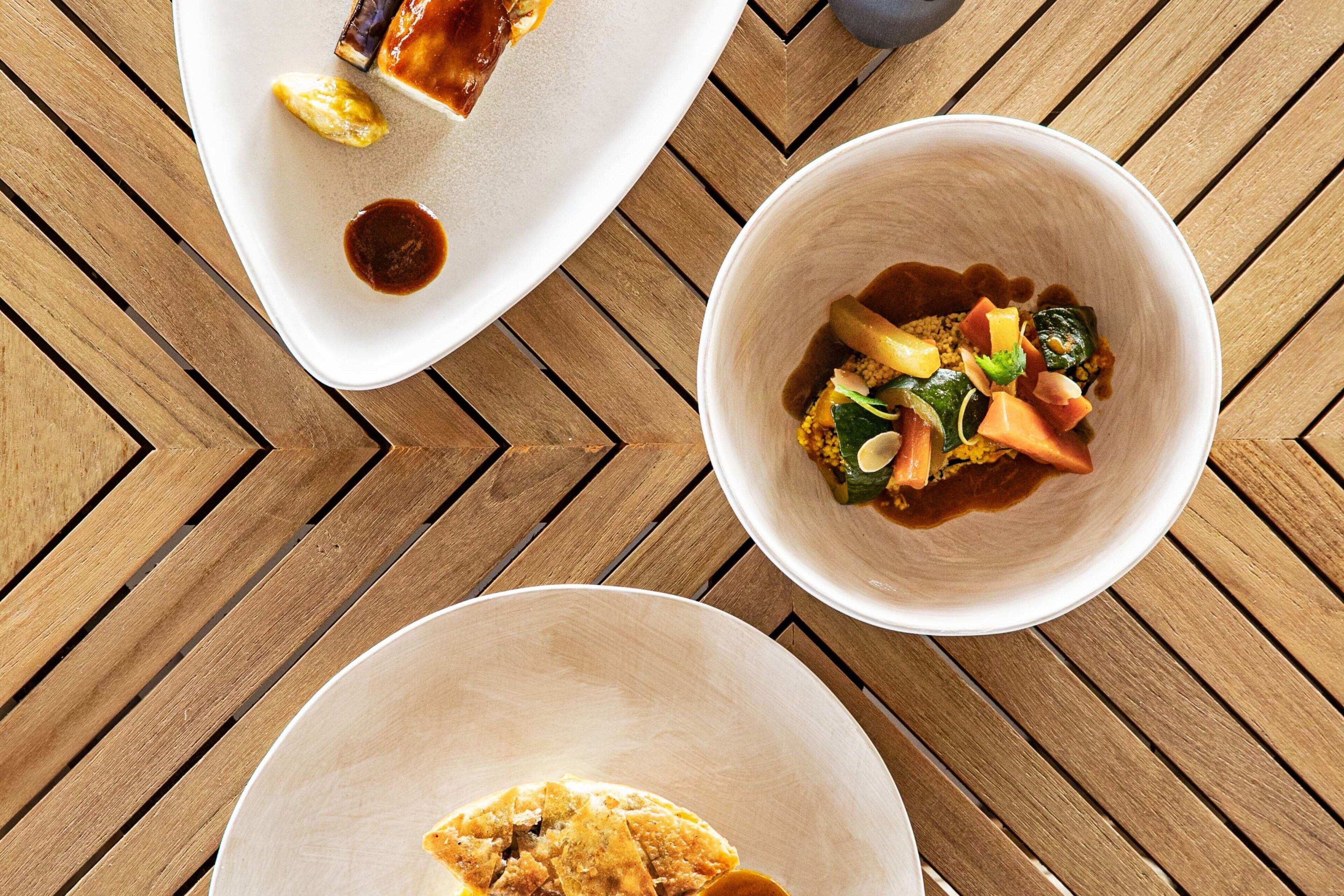 A wooden table with three white plates containing various dishes.