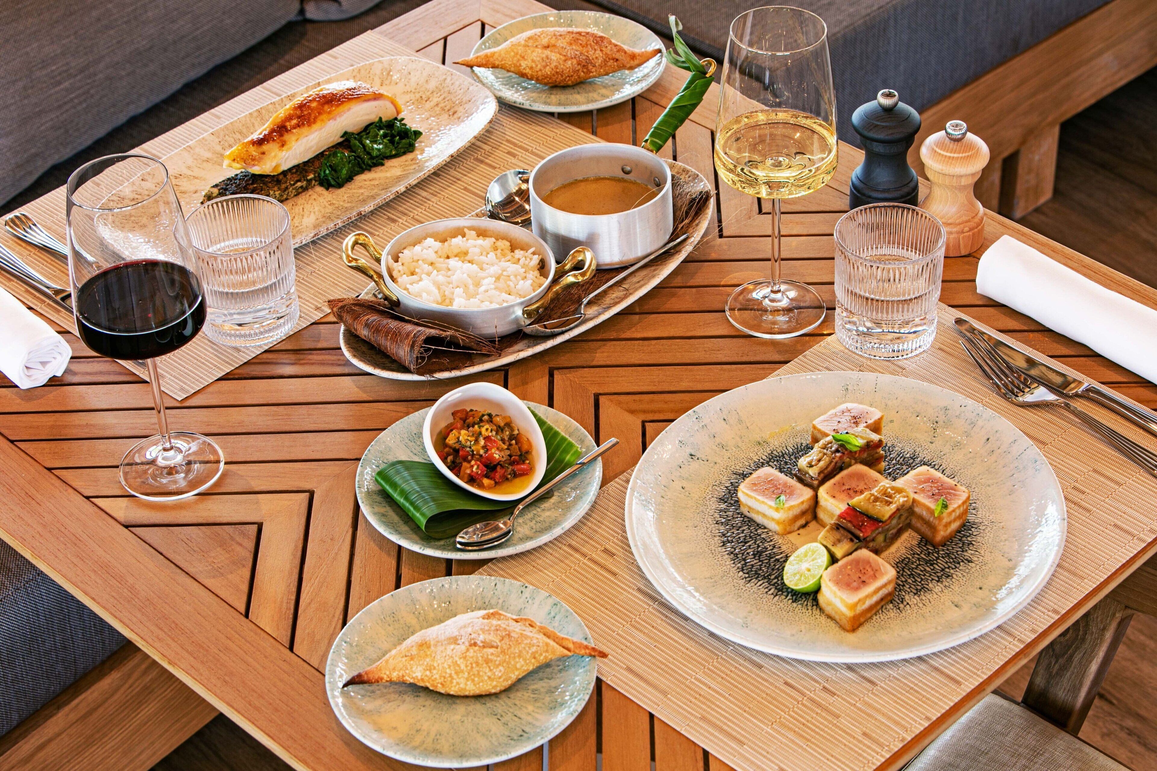A wooden dining table with various dishes, glasses of wine, and cutlery.