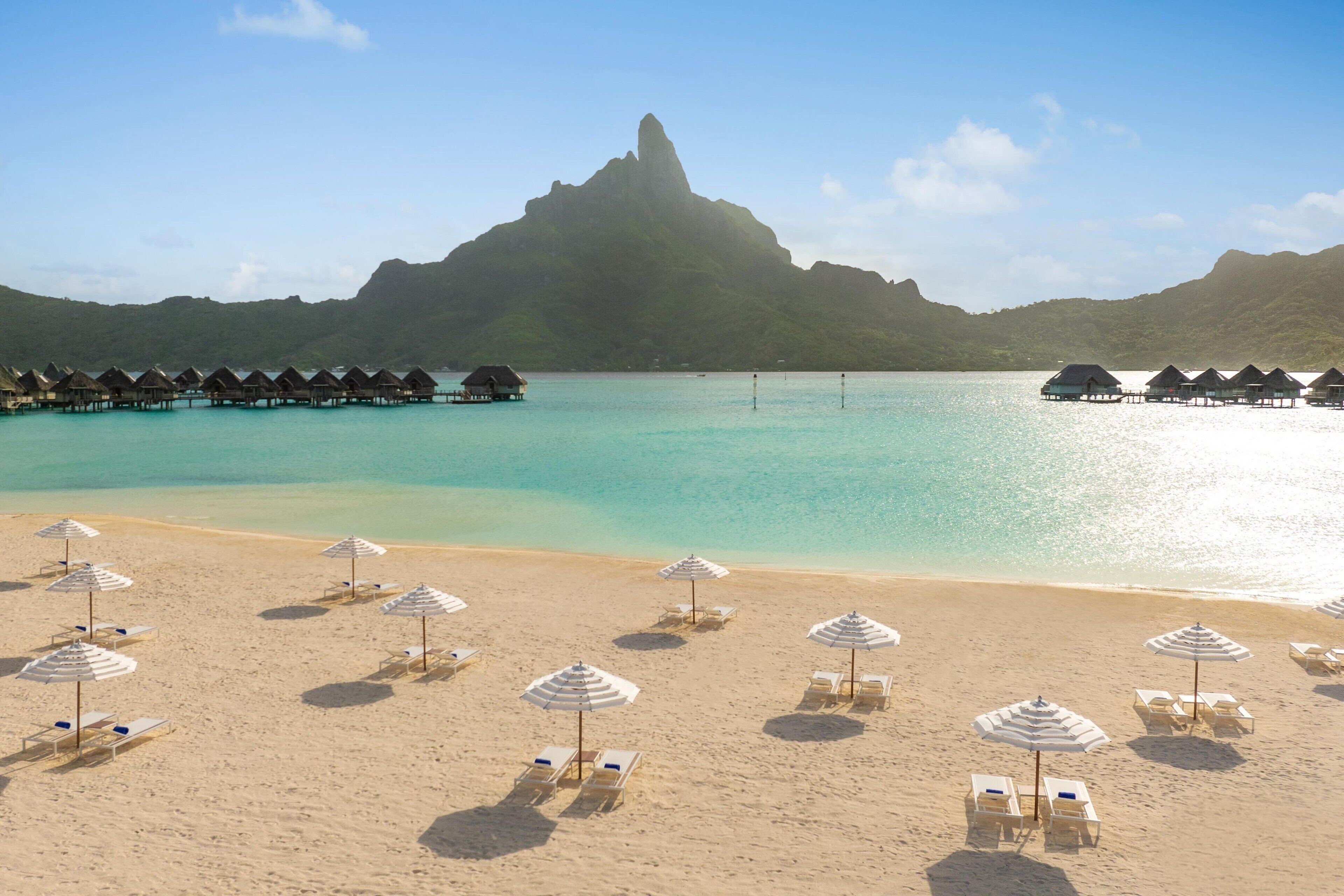 A beach with overwater bungalows and beach umbrellas.