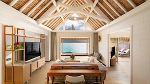 A spacious living room with a high ceiling, a large window offering a view of the sea, a wooden coffee table, and a seating area with a sofa and chairs. - The Westin Bora Bora Resort & Spa (Bora Bora)