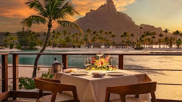 A dining table set for two with a view of a mountain and beach.