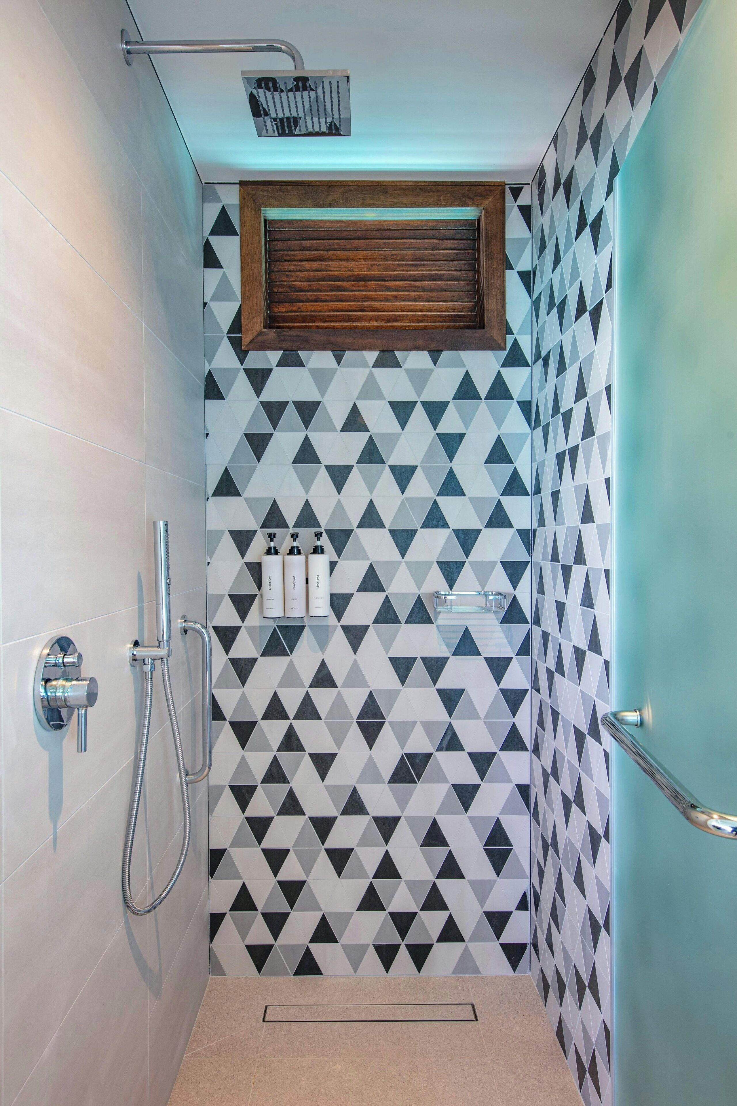 A modern bathroom with geometric patterned tiles, a shower area, and a wooden window.