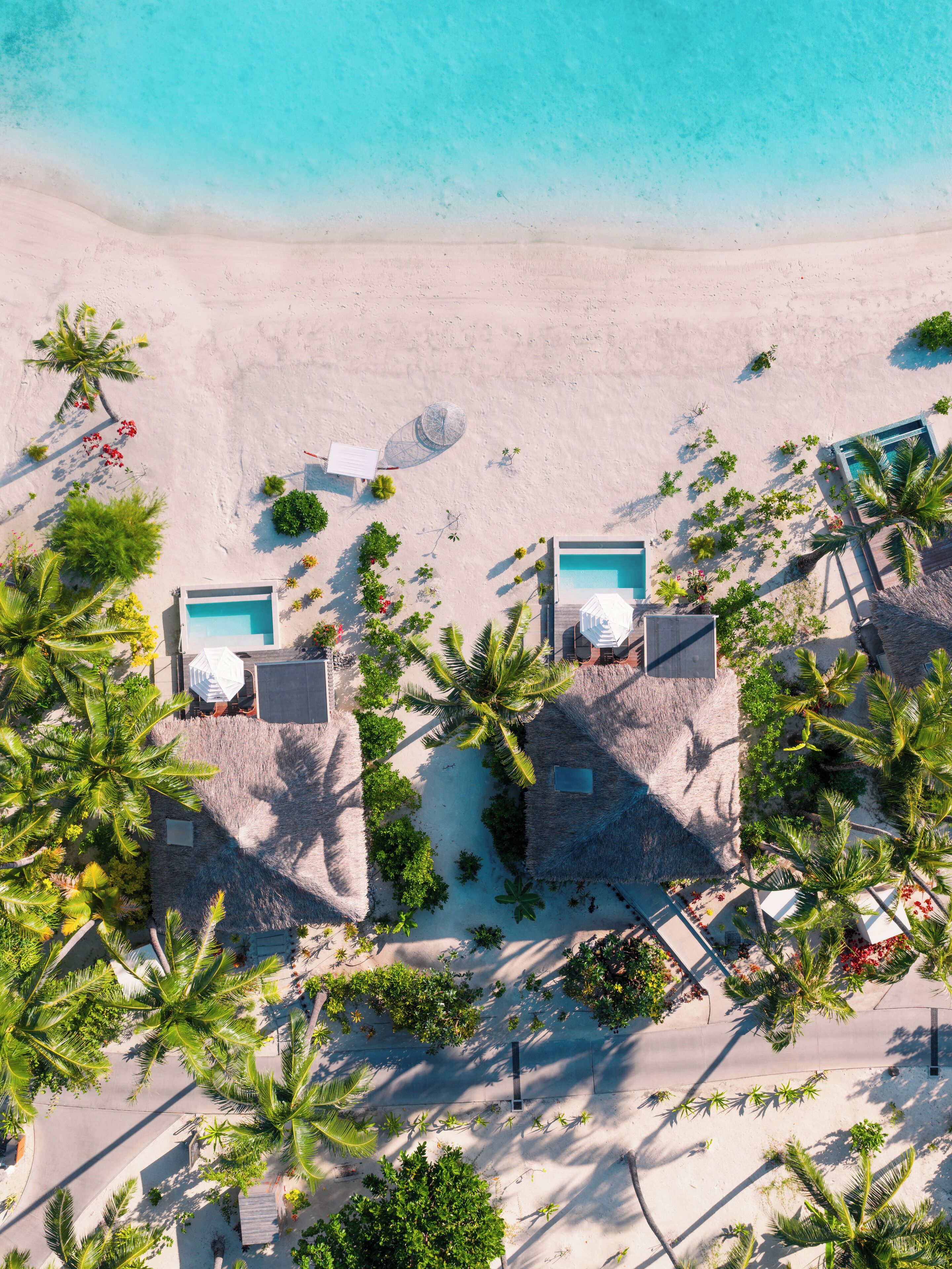 An aerial view of a beach resort with two pools, palm trees, and a sandy beach.