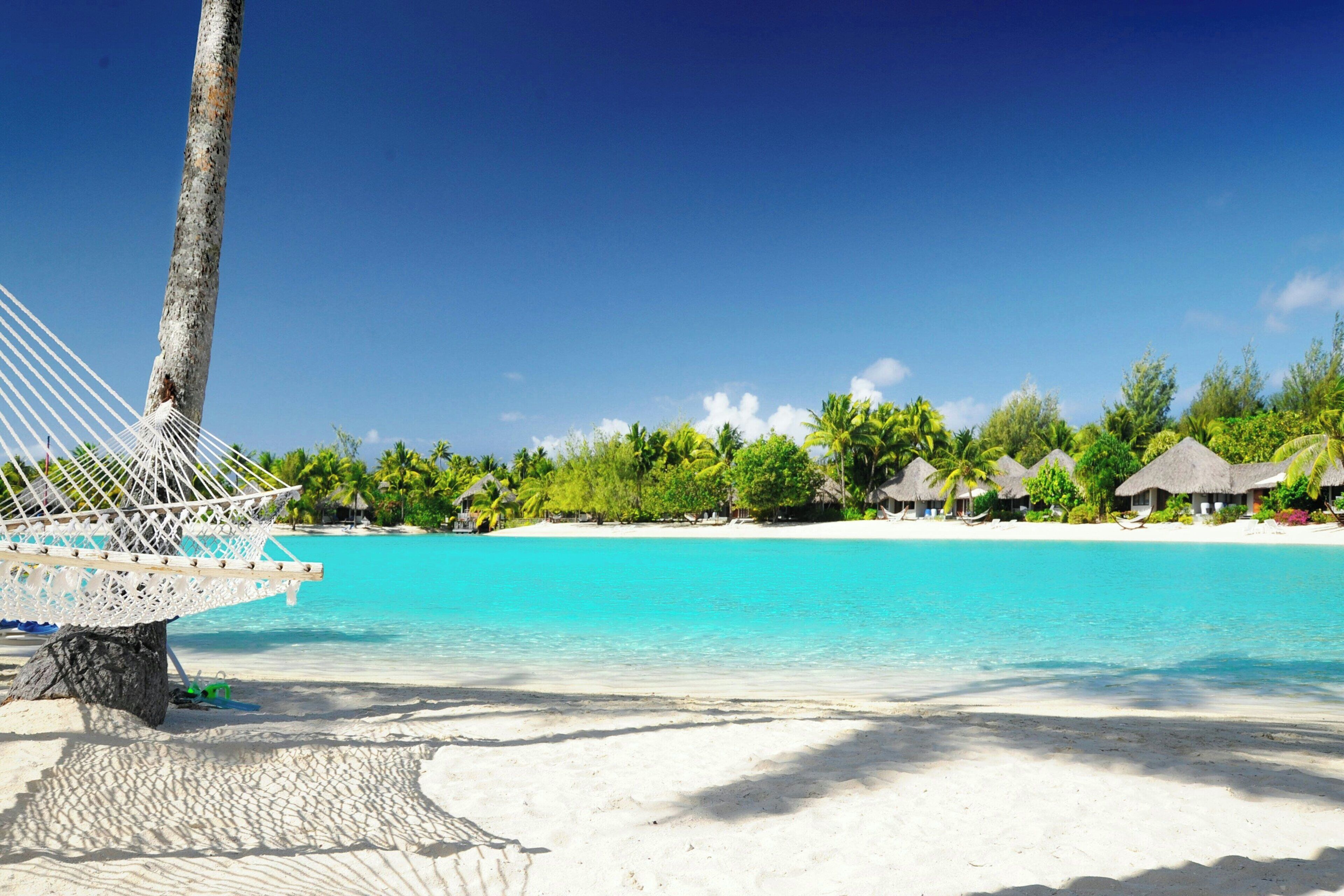 A beach with clear turquoise water, white sand, and overwater bungalows with thatched roofs.