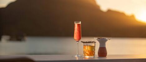 Un bar avec un verre à cocktail et une carafe posés sur le comptoir, et un coucher de soleil en arrière-plan.
