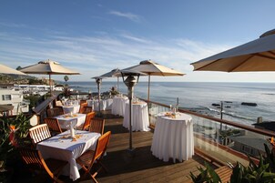 A seaside dining area with tables set for guests, overlooking the ocean.