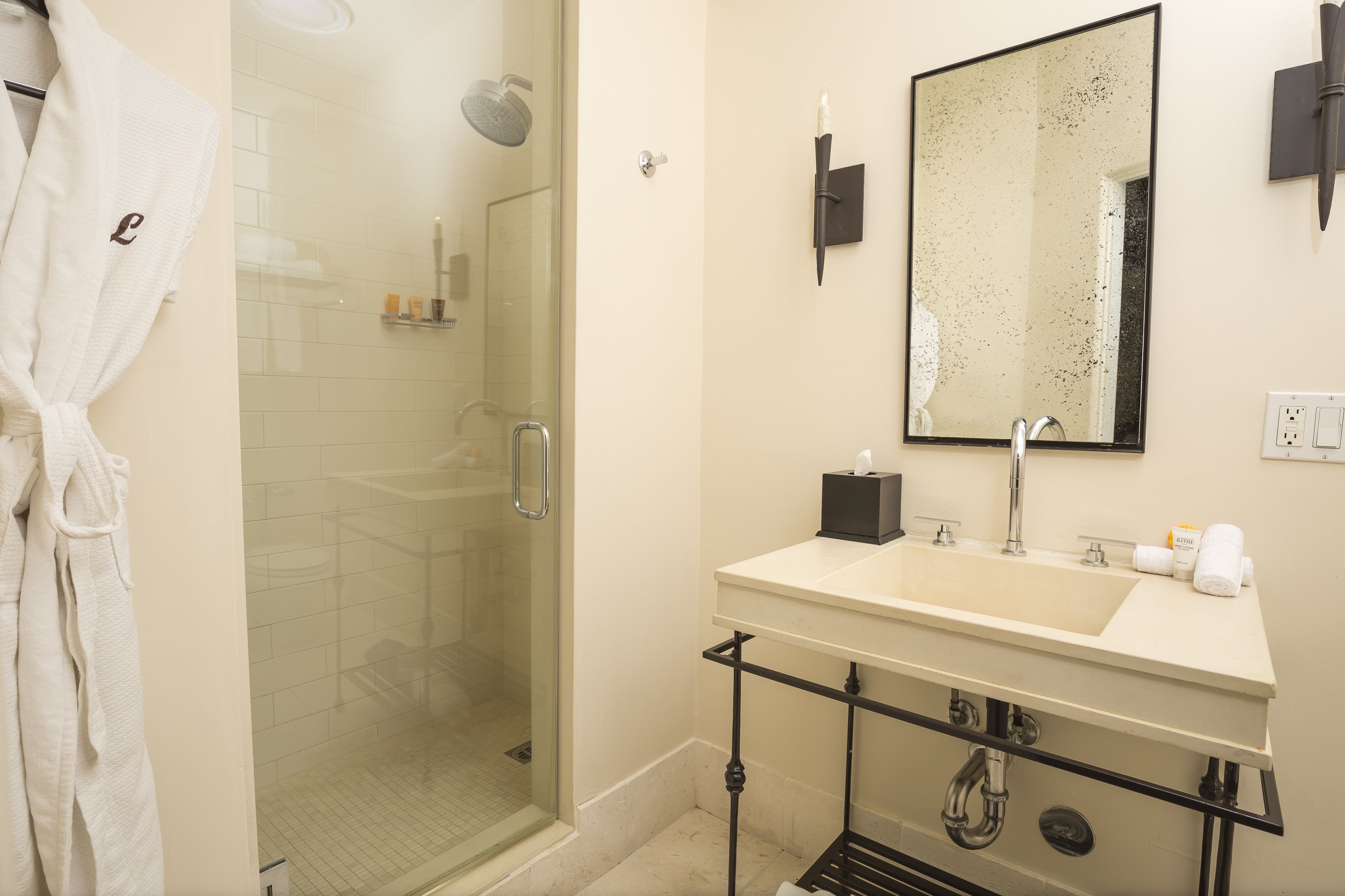 A bathroom with a glass-enclosed shower, a white sink with a black soap dispenser, and a mirror with a decorative frame.