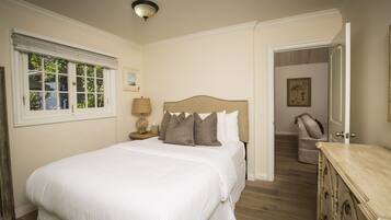 A bedroom with a large bed, a nightstand with a lamp, a door leading to another room, and a dresser.