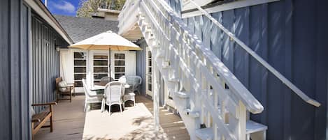 A wooden deck with a white staircase, a covered seating area with chairs, and a table.