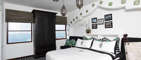 A bedroom with a large bed, a wardrobe, a chair, and a view of the sea through a window.