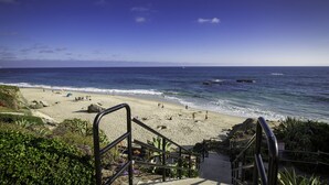 Una playa con una escalera que baja hacia la orilla, rodeada de vegetación.