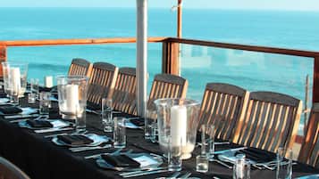 A table set for dining with a view of the ocean, a table lamp, and wooden chairs.
