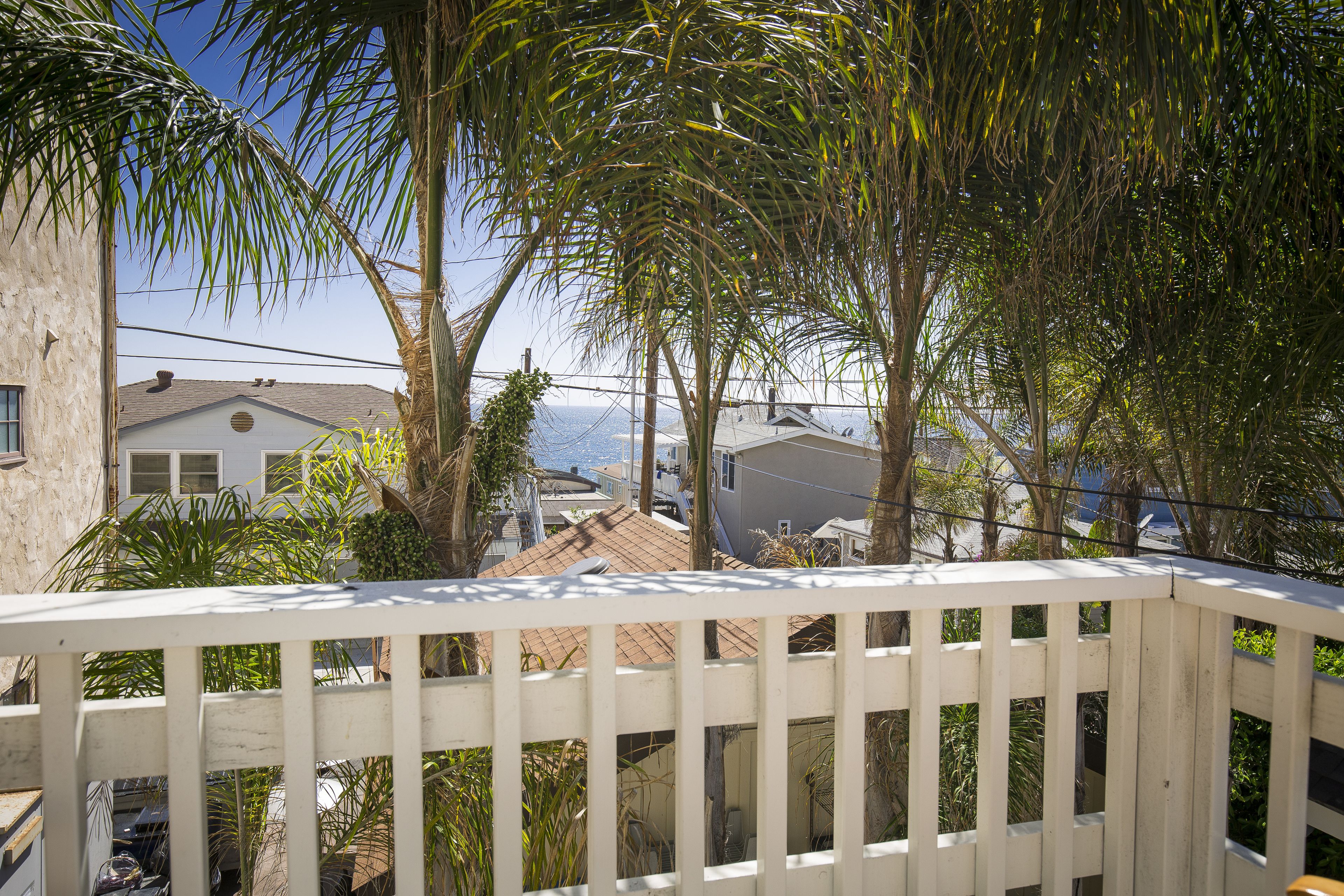 A balcony with a white railing overlooking a residential area with houses and palm trees.