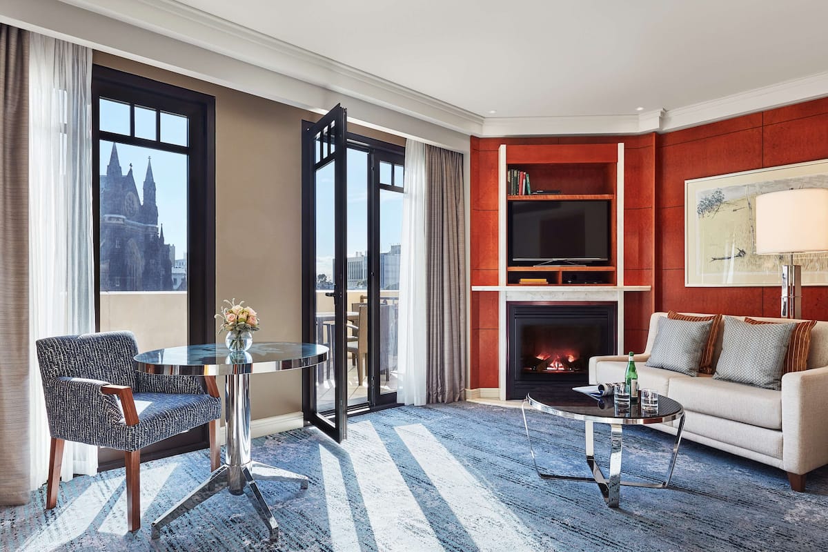A hotel room with a modern living area, a fireplace, a television, and a large window with a city view.