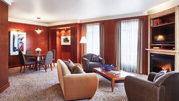 A well-appointed living room with a sofa, armchairs, a coffee table, a fireplace, a television, and a bookshelf.