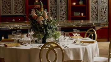 A round dining table with a white tablecloth, gold chairs, and a centerpiece of flowers and greenery.