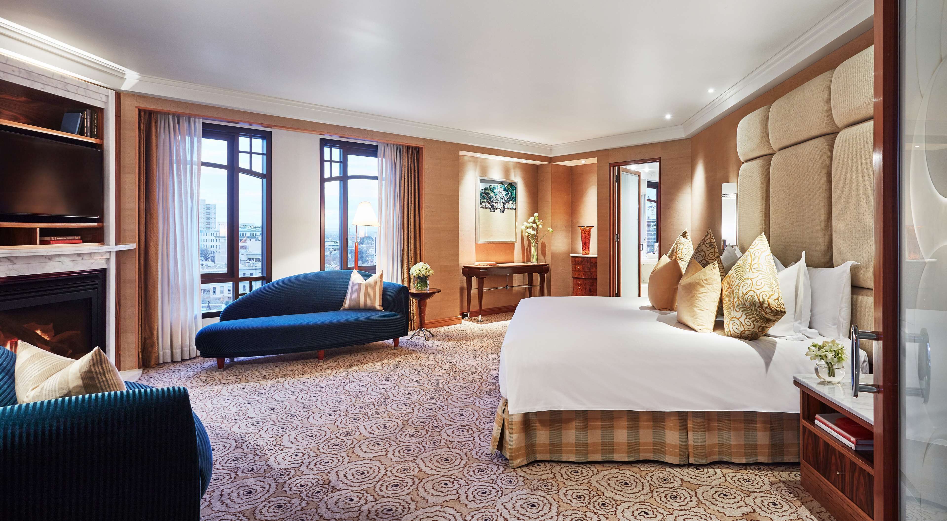 A hotel room with a large bed, a sofa, a television, and a fireplace.