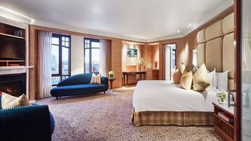 A hotel room with a large bed, a sofa, a television, and a fireplace.