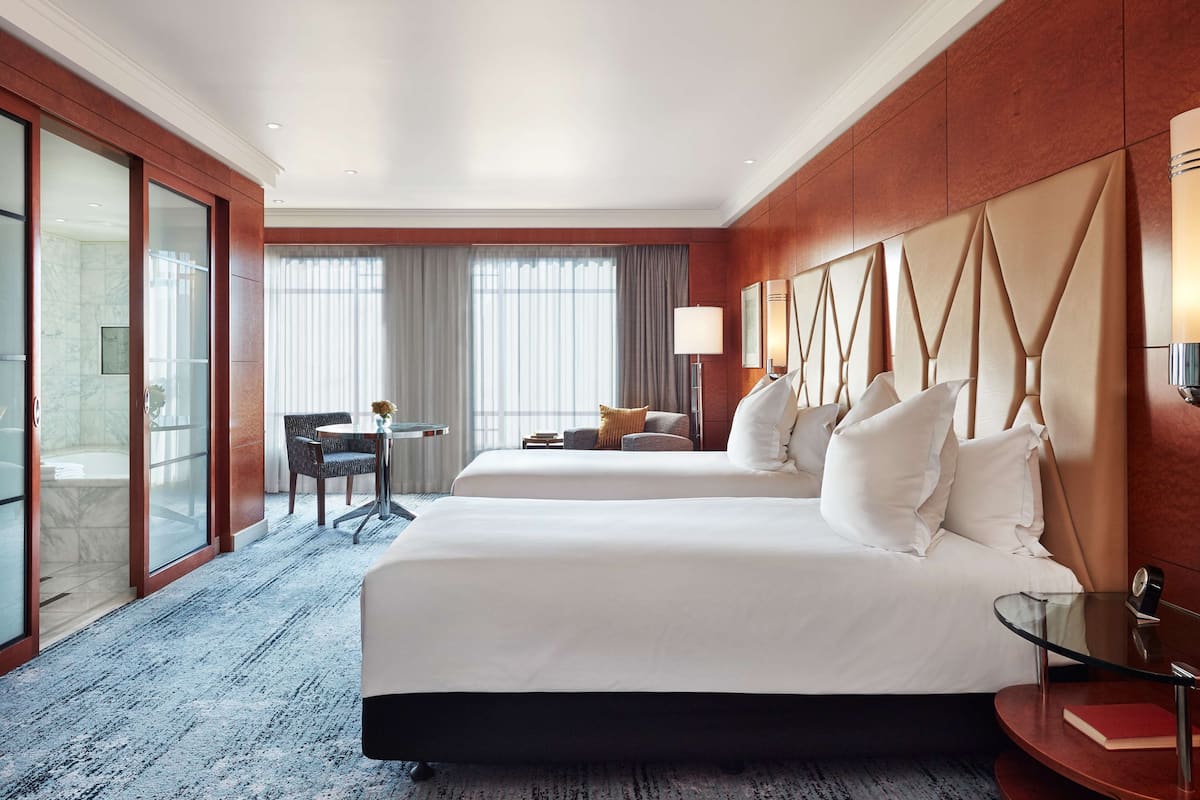 A hotel room with two beds, a desk, a chair, and a large window with curtains.