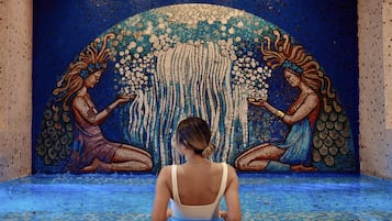 Un mur décoré d’une mosaïque représentant deux personnages et une cascade.