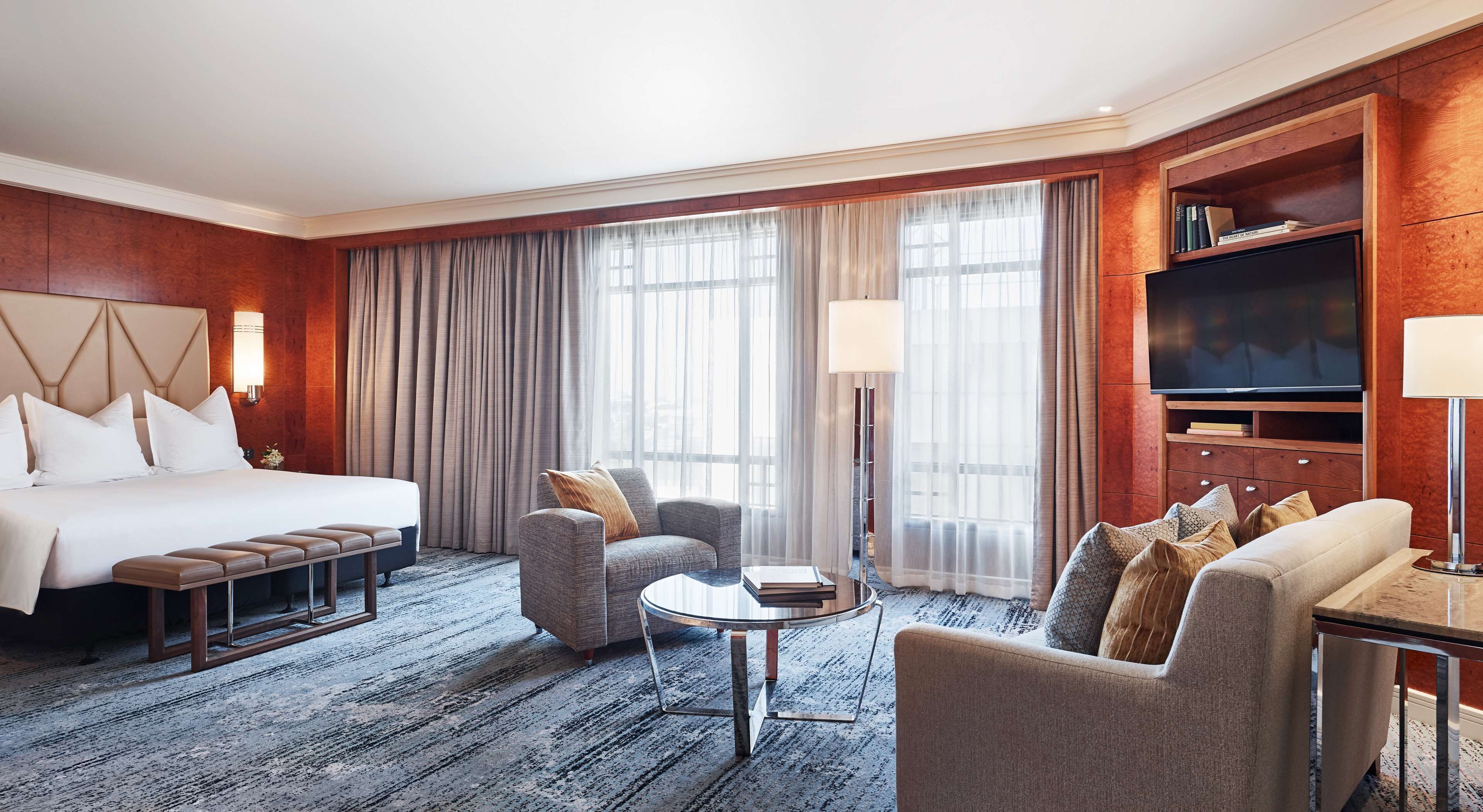 Ein Hotelzimmer mit einem großen Bett, zwei Sesseln, einem Couchtisch, einem Fernseher und einem Bücherregal.