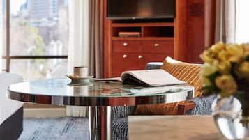 A modern hotel room with a glass-top table, a book, a remote control, and a television set against a wooden cabinet.