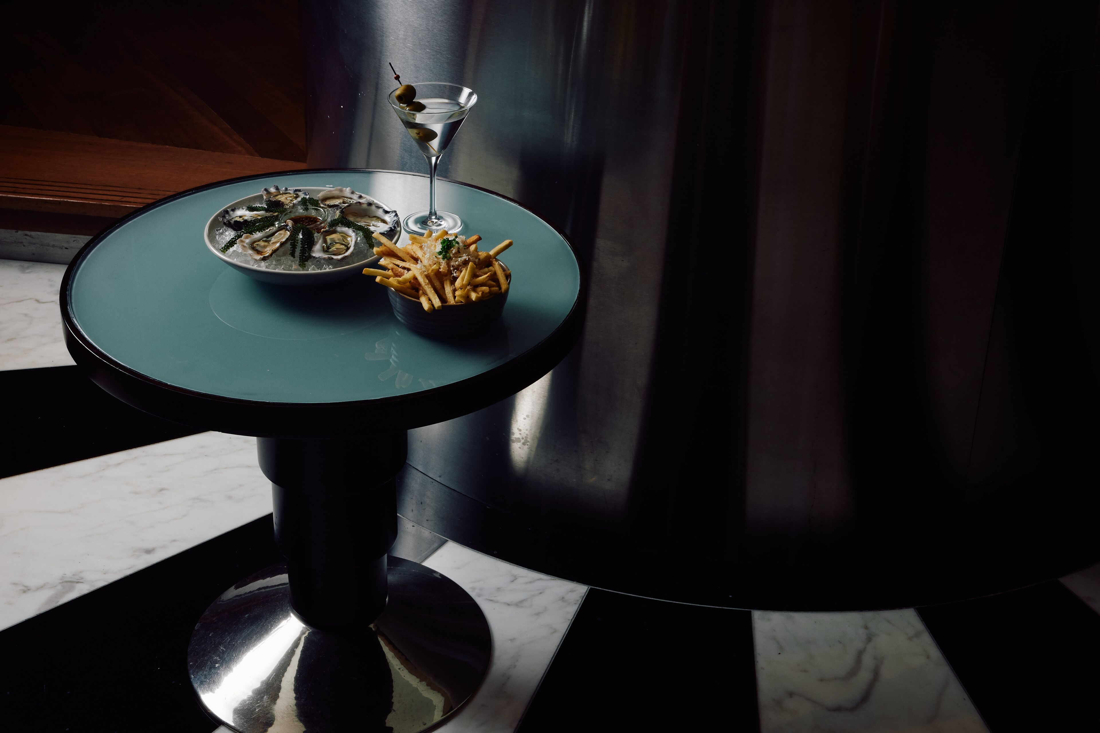 A table with a plate of oysters, a martini glass, and a bowl of fries.