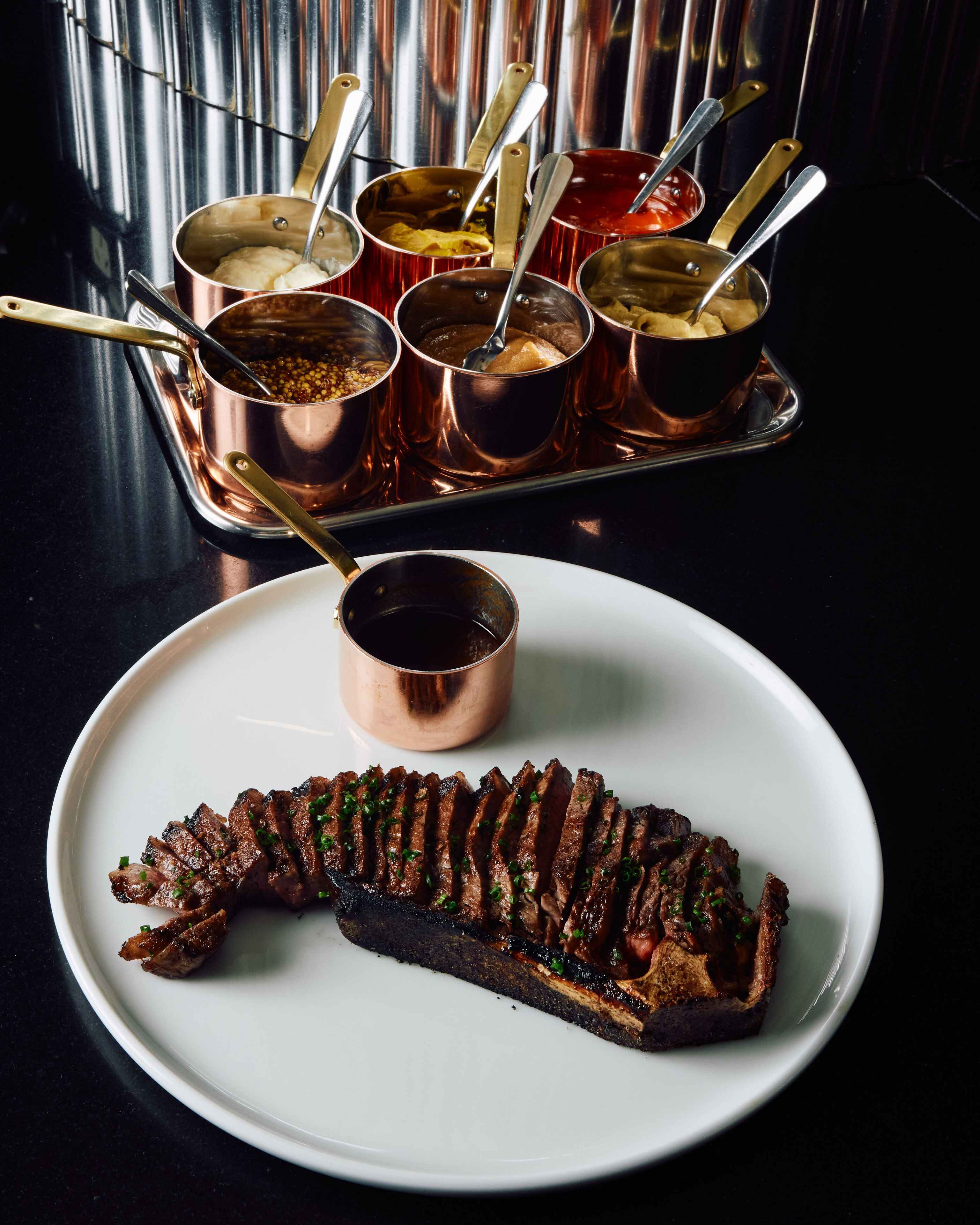 A plate of sliced meat with a side of sauce and a tray of sauces.