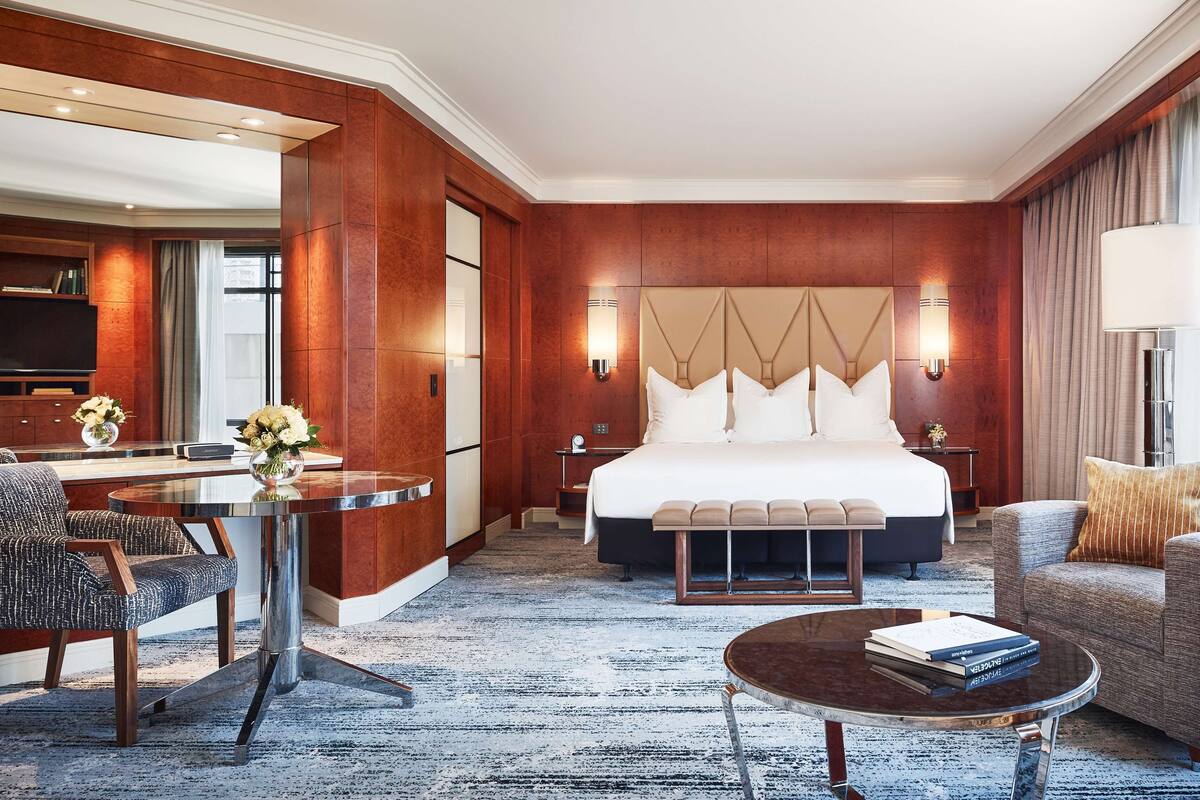 A hotel room with a large bed, a sitting area with a coffee table, a desk with a chair, and a view of the city.