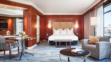 A hotel room with a large bed, a sitting area with a coffee table, a desk with a chair, and a view of the city.