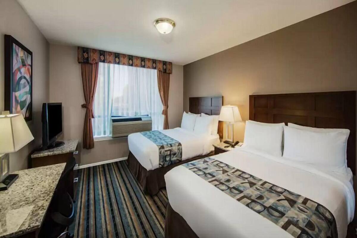 Habitación de hotel con dos camas, un escritorio, un televisor y una ventana con cortinas.