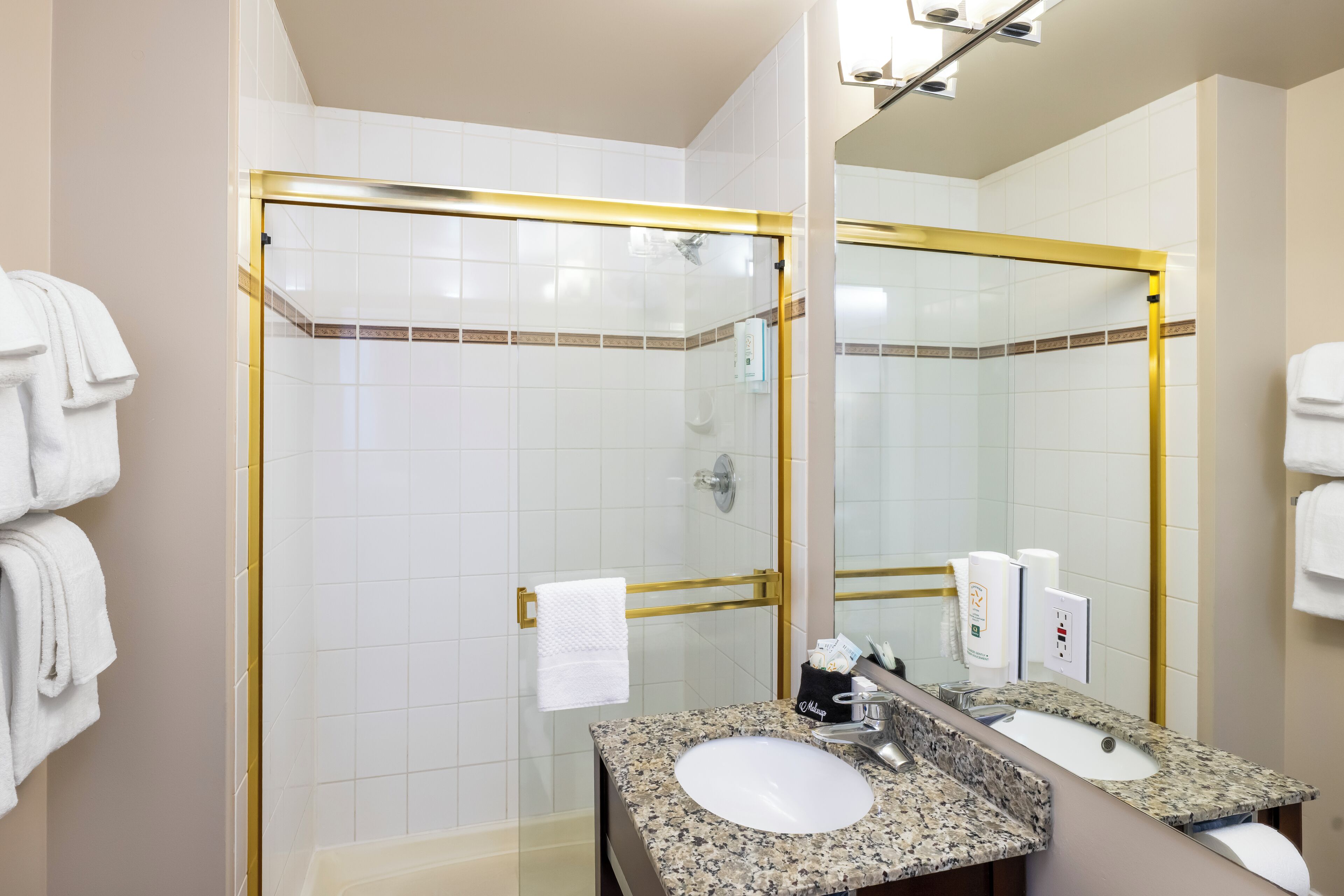 A bathroom with a glass-enclosed shower, a sink with a granite countertop, and a mirror with a gold frame.