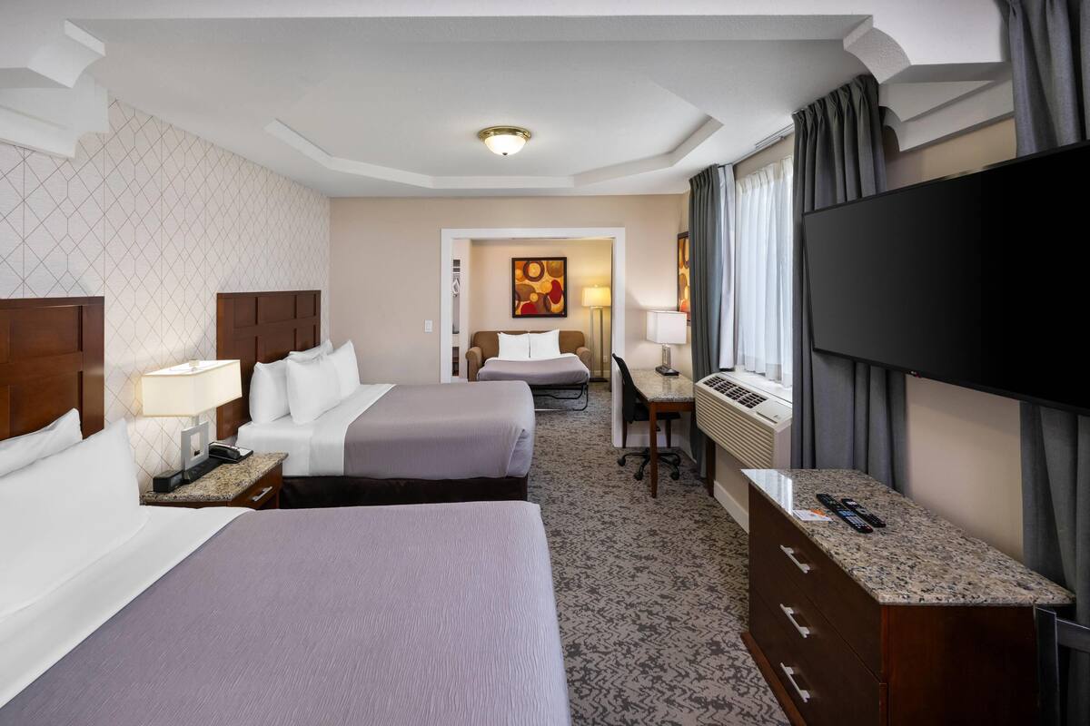 Habitación de hotel con dos camas, un escritorio, un televisor y una ventana con cortinas.