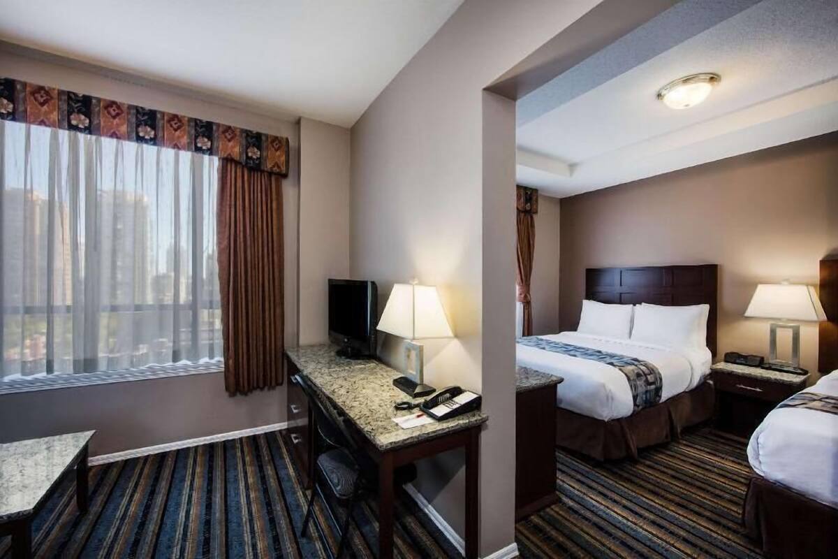 Ein Hotelzimmer mit Schreibtisch, zwei Betten, einem Fernseher und einem Fenster mit Vorhängen.