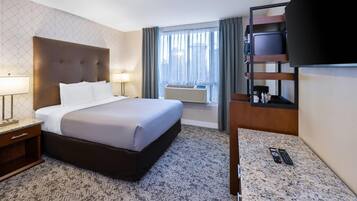 Habitación de hotel con cama, lámparas de noche, televisión, escritorio con control remoto y ventana con cortinas.