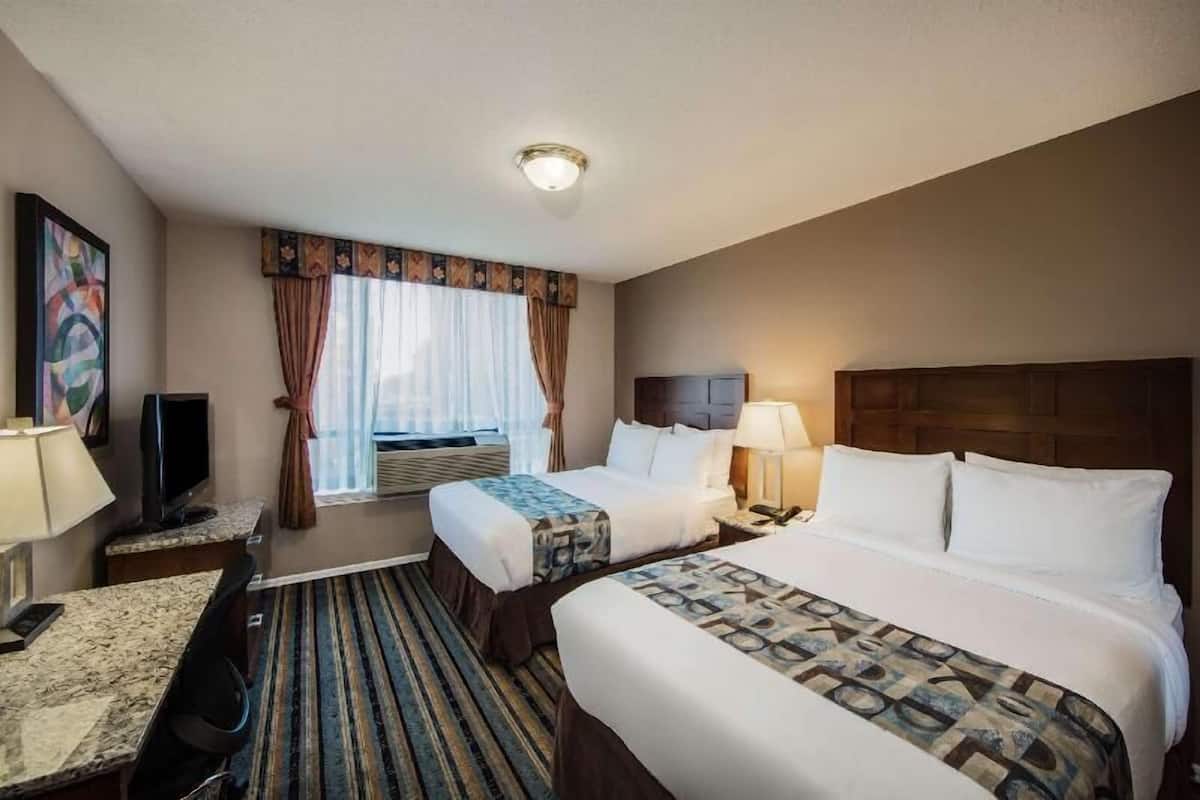 Ein Hotelzimmer mit zwei Betten, einem Schreibtisch, einem Fernseher und einem Fenster mit Vorhängen.