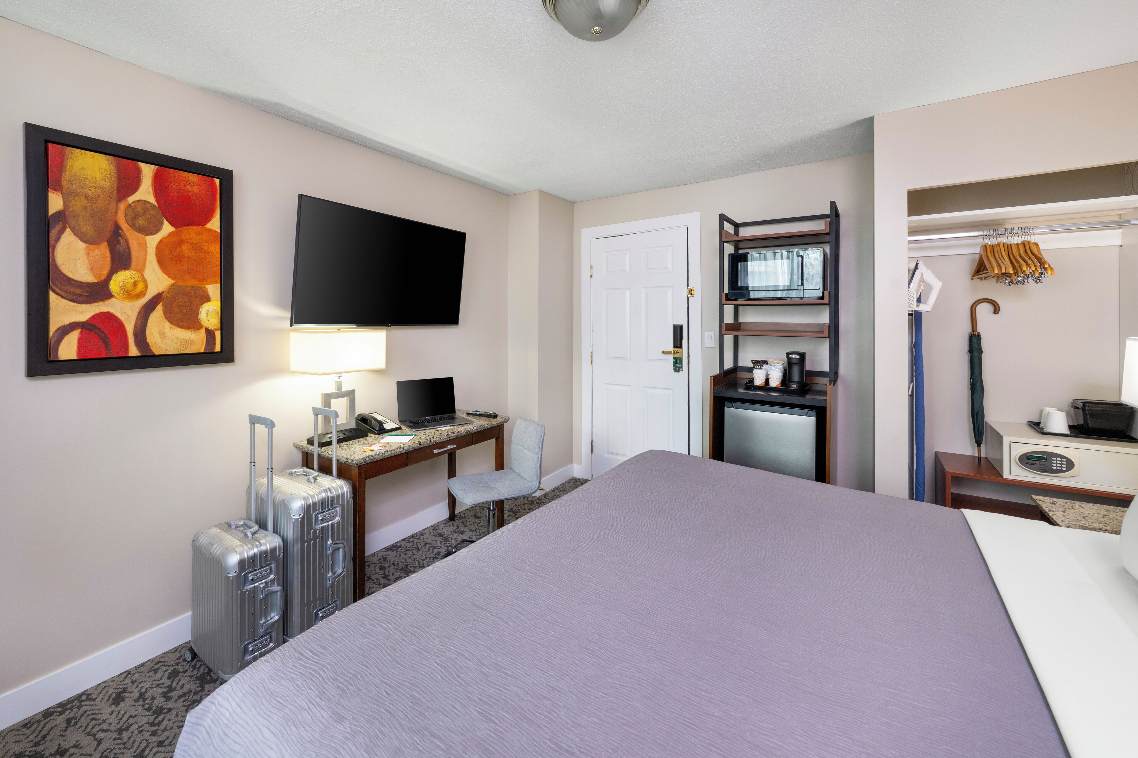 Una habitación de hotel con cama, escritorio, silla, televisión y perchero.