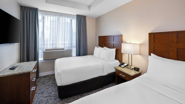 A hotel room with two beds, a TV, a desk, a lamp, and a window with curtains.