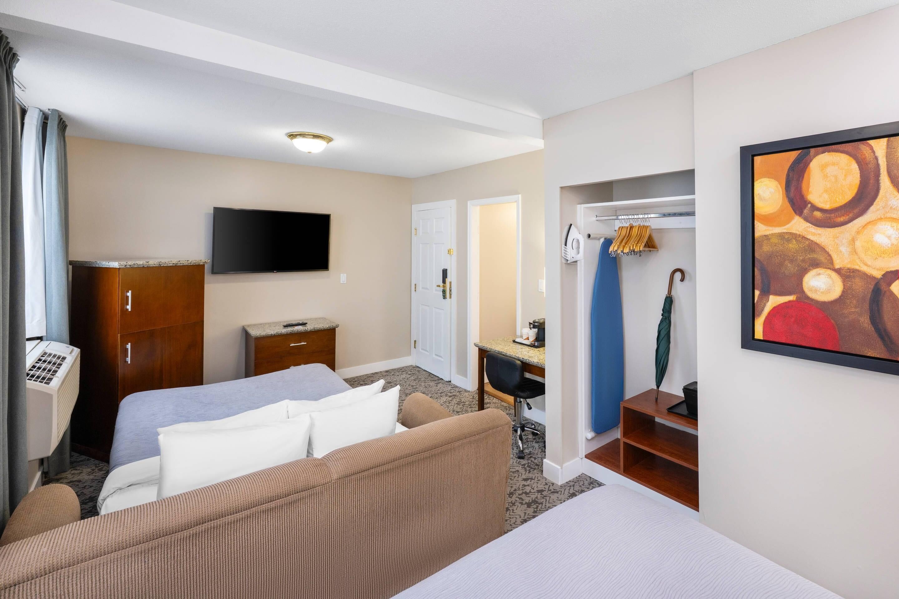Una habitación de hotel con cama, escritorio, televisión, armario y un cuadro en la pared.