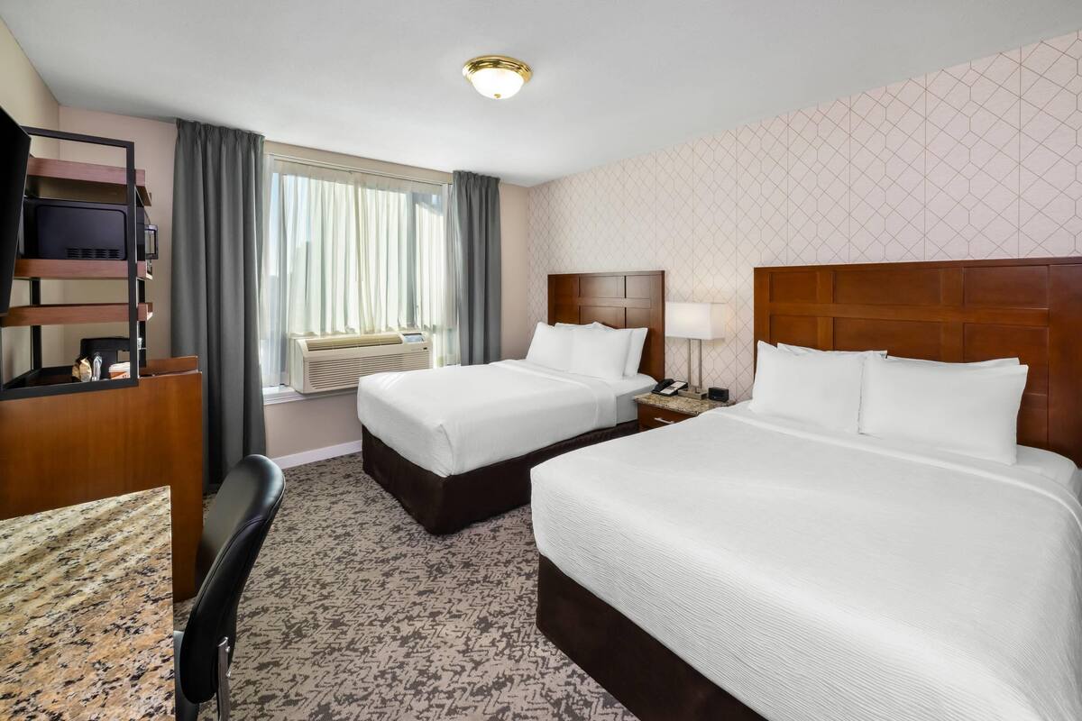 Habitación de hotel con dos camas, un escritorio, una silla, una lámpara de escritorio y una ventana con cortinas.